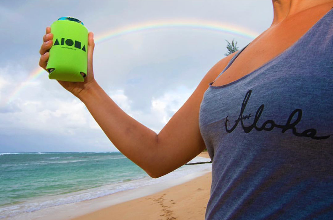 Girl holding an Aloha Shapes ® logo koozie on the beach in front of a rainbow