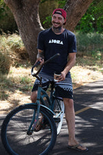 Person smiling riding a beach cruiser bike wearing an Aloha Island Shapes logo t-shirt
