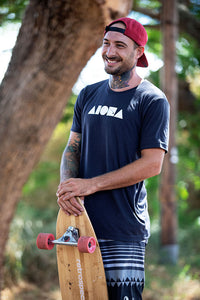 Person smiling holding a longboard skateboard wearing an Aloha Island Shapes logo t-shirt