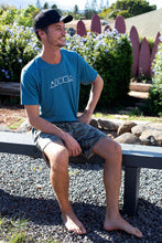 Man sitting on a bench wearing Mauka to Makai Unisex sueded jersey tee in blue