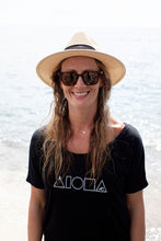 Woman wearing straw hat and black Mauka to Makai Aloha Shapes womens slouchy tee on a beach in Maui Hawaii  Edit alt text