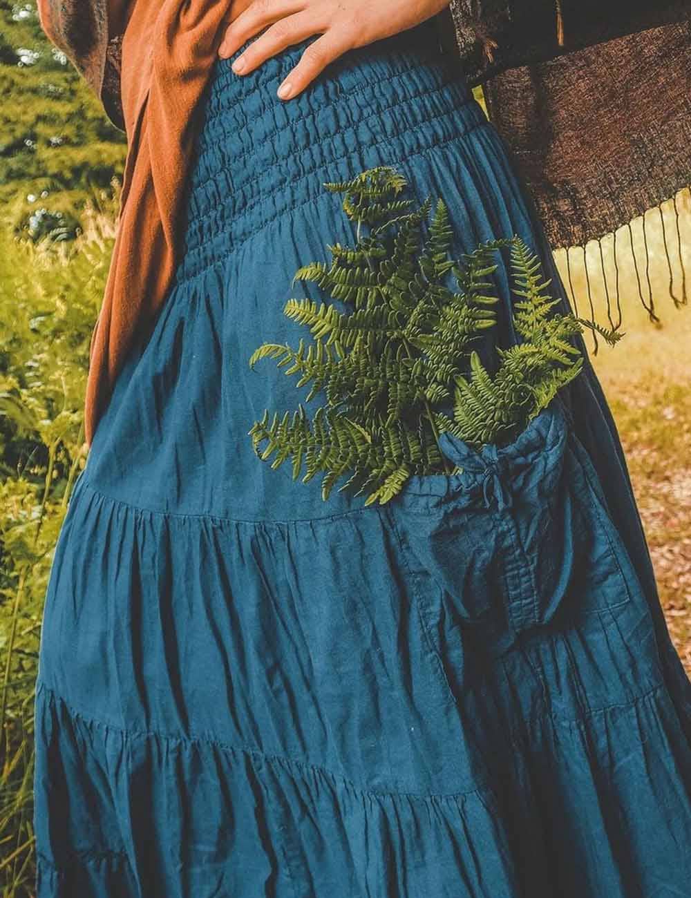 Person wearing a blue dress with green fern embroidery in a natural setting