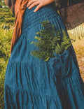 Person wearing a blue dress with green fern embroidery in a natural setting