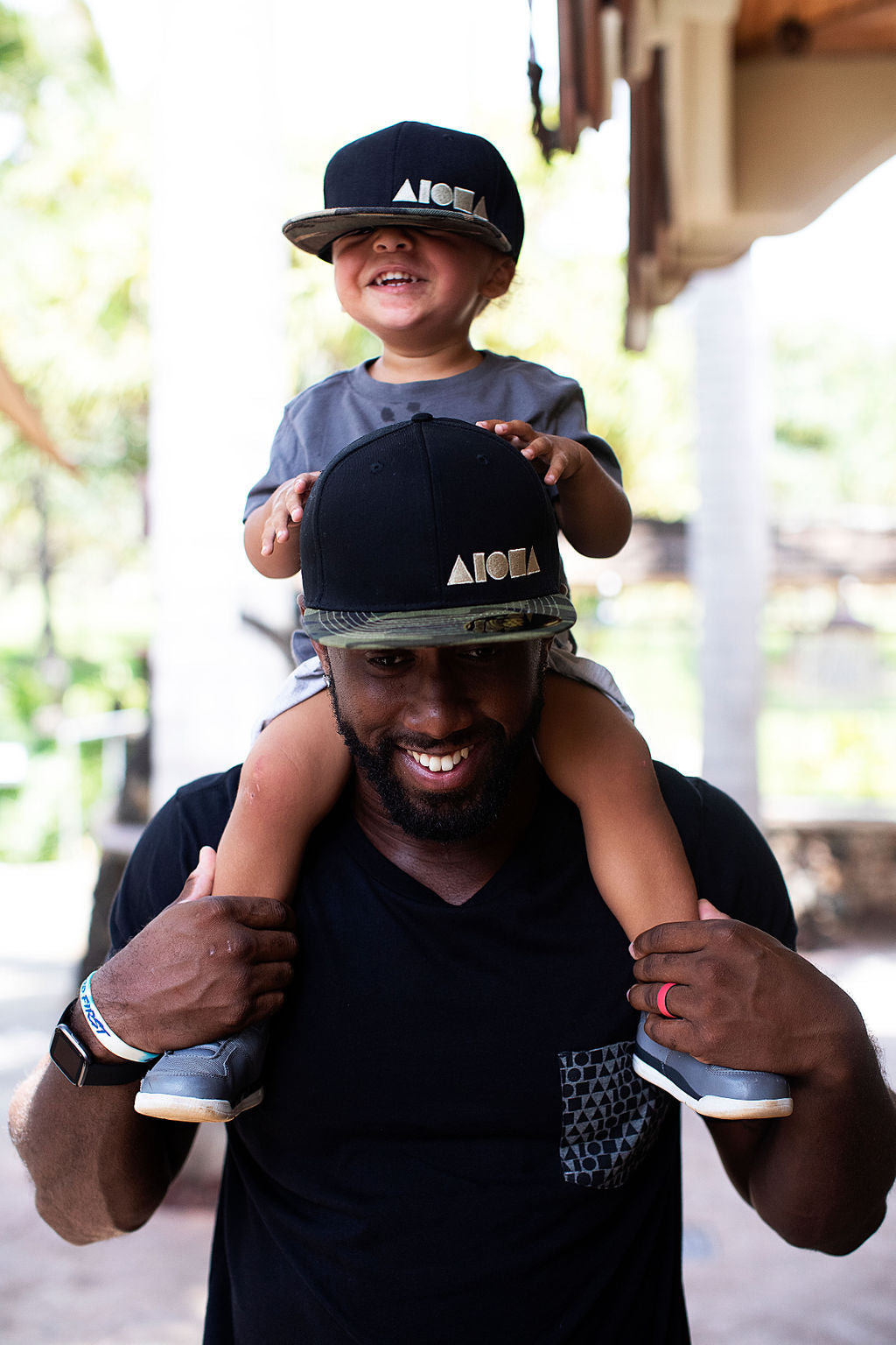 Father with son on shoulders wearing matching snapback hats. Father is wearing The Hunt Is On camo bill snapback