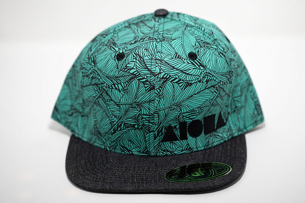 Turquoise adult flat brim snapback hat with black tropical banana leaf pattern. Embroidered with black Aloha Shapes ® logo