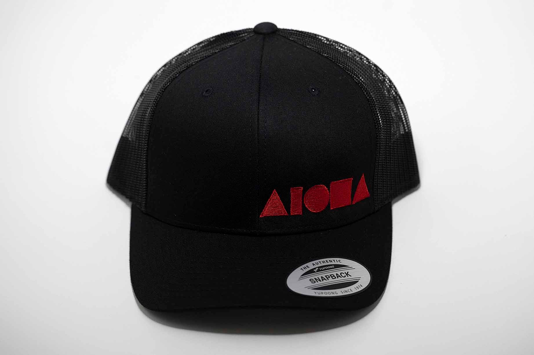 Aloha Shapes ® logo embroidered in red on an all black curved bill/mesh back snapback hat.