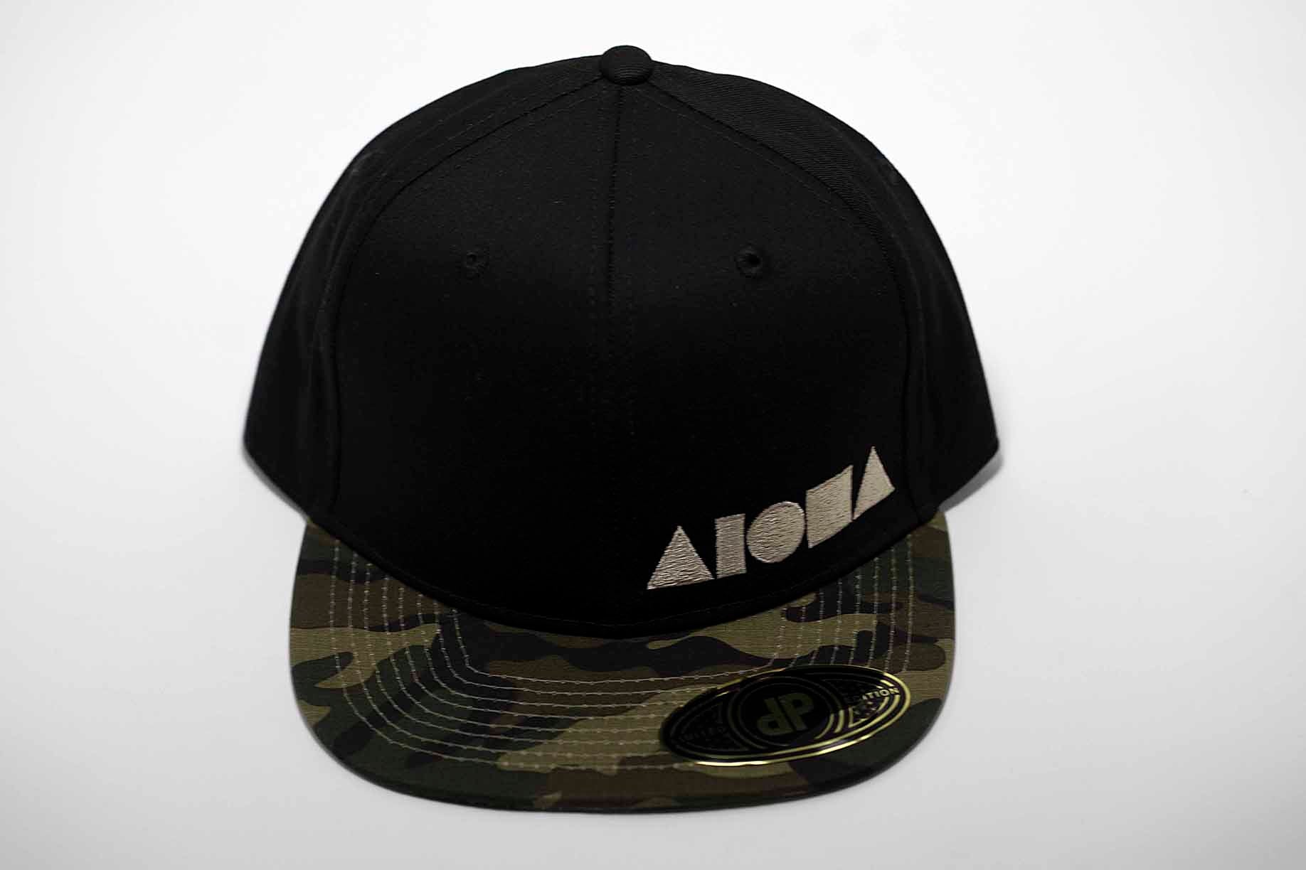 Black adult flat brim snapback hat embroidered with tan Aloha Shapes ® logo and a camo brim