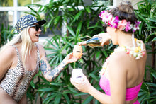 Two happy girls celebrating with wine wearing leis and our "Pineapple Party" Aloha Shapes ® snapback