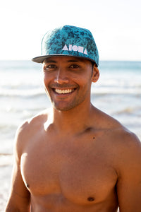 Handsome young man with no shirt wearing an ALOHA Shapes ® logo snapback hat on the beach. 
