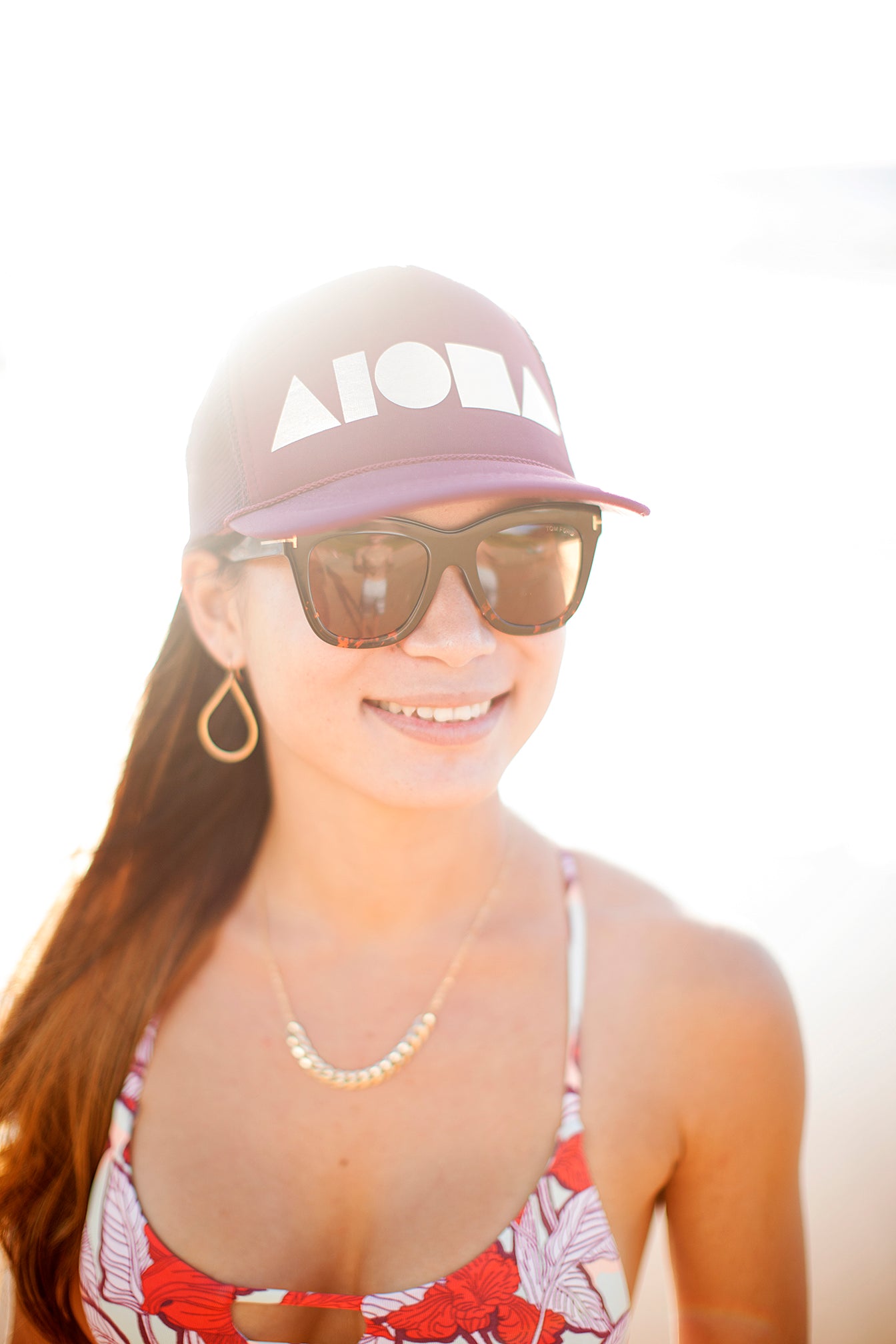 Young woman in the sunlight wearing an ALOHA Shapes ® logo maroon/silver trucker hat.