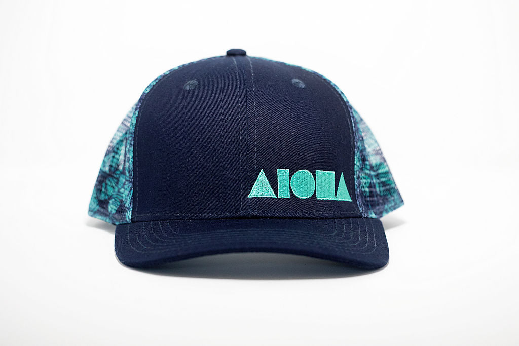 Adult curved bill snapback hat with navy blue front panels and teal colored kalo leaves printed on back mesh panels. Embroidered on front with teal Aloha Shapes ® logo