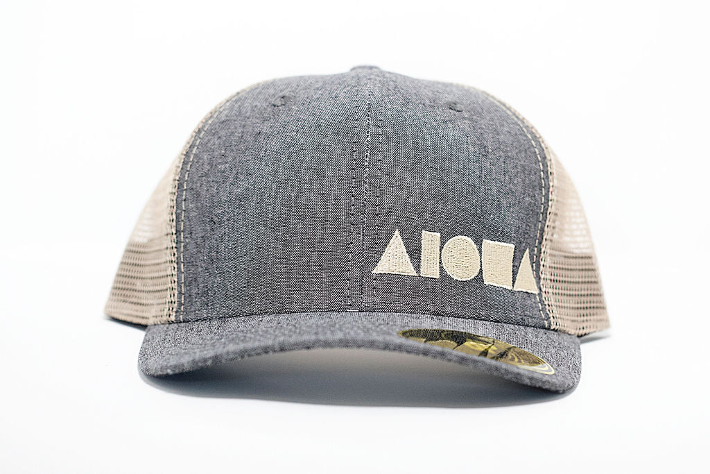 Adult curved bill snapback with grey denim bill and front panels, cream color back mesh panels. Embroidered on front with cream Aloha Shapes logo