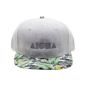 Adult flat brim snapback hat. Banana print fabric flat brim. Grey denim panels. silver embroidered Aloha Shapes® logo.