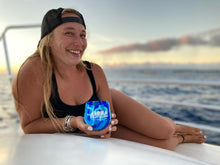 Woman sitting on boat with Hawaii sunset in background smiling holding a Soley Aloha silicone beach cup