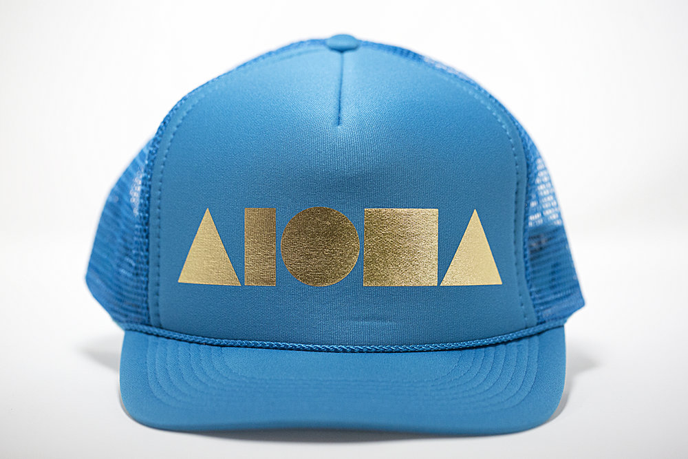 Adult foam trucker hat. Turquoise brim, front foam panel and mesh back panels. Foil printed with gold ALOHA Shapes ® logo