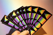 Hand fanning out multiple Ombre Rainbow Aloha Shapes decal stickers in front of a rainbow photo