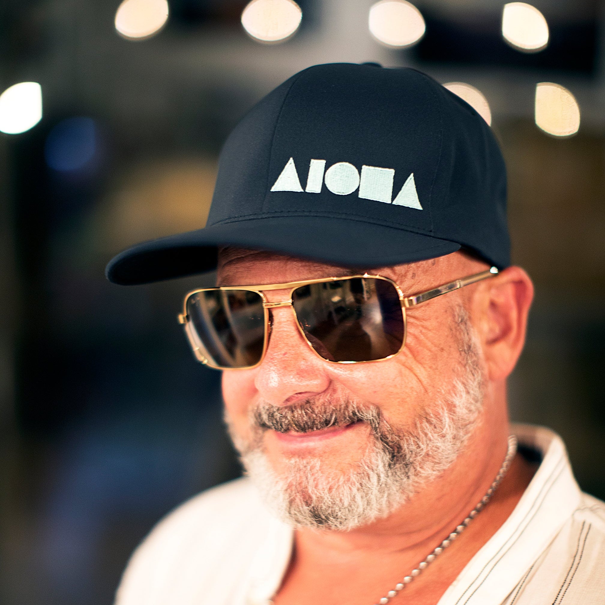 Older gentleman wearing an ALOHA Shapes ® logo Flexfit hat and dark sunglasses