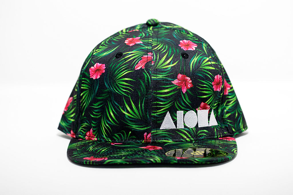 Adult flat brim snapback hat with deep green leaves and red flowers. Embroidered with white Aloha Shapes ® logo