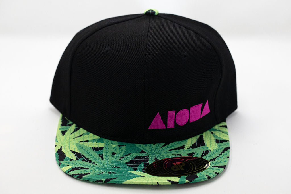 Black canvas flatbrim snapback with satin fabric print on brim with green pakalolo leaves and a pink embroidered Aloha Shapes logo