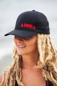 Young blond dreadlocked girl wearing an ALOHA Shapes ® logo Flexfit hat on the beach