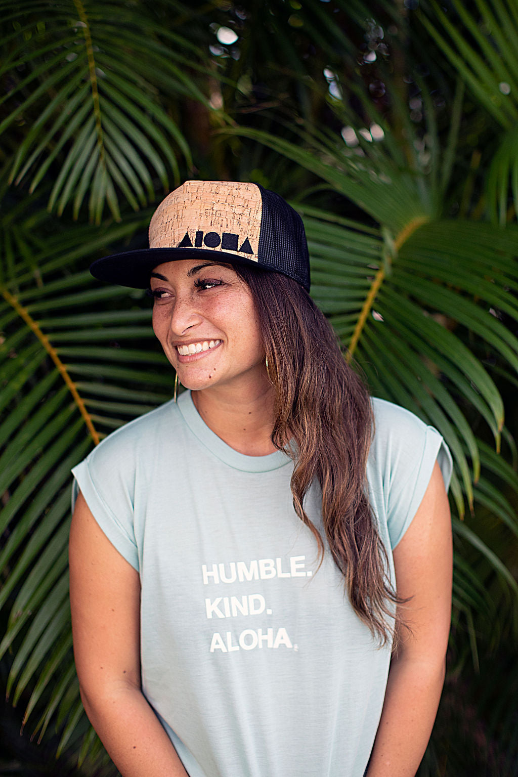 Woman wearing mint green flowy muscle tee printed with "Humble. Kind. Aloha" on front chest in white