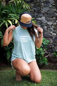 Woman wearing mint green flowy muscle tee printed with "Humble. Kind. Aloha" on front chest in white