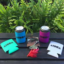Assortment of Aloha Shapes ® logo koozies spread out in front of tropical foliage