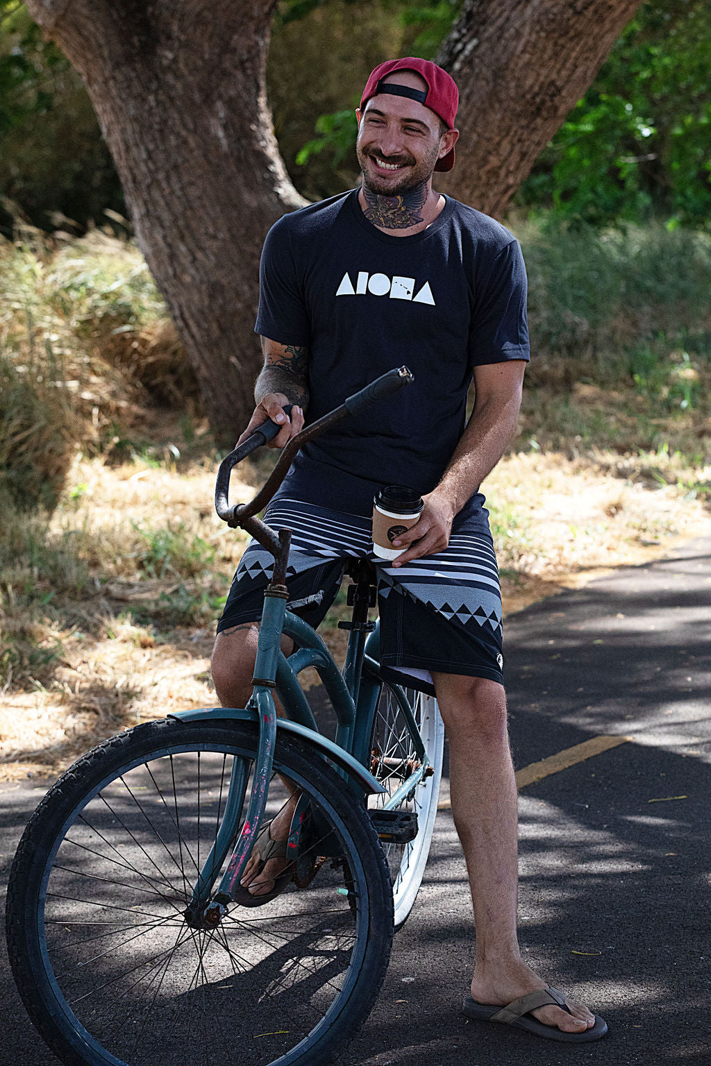 Person smiling riding a beach cruiser bike wearing an Aloha Island Shapes logo t-shirt