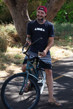 Person smiling riding a beach cruiser bike wearing an Aloha Island Shapes logo t-shirt