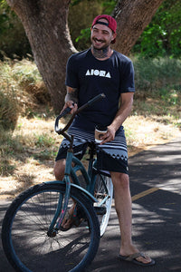 Person smiling riding a beach cruiser bike wearing an Aloha Island Shapes logo t-shirt