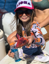 Young girl on a fishing boat holding a Hawaiian fish wearing pink and white Aloha Shapes ® logo youth trucker hat