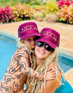 Mom and daughter wearing matching Maroon and Gold Mauka to Makai aloha shapes logo trucker hats