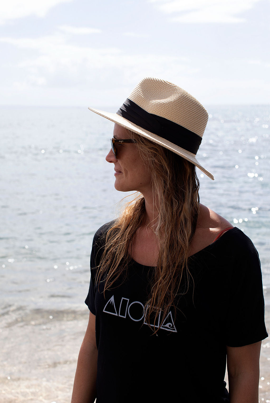 Woman wearing straw hat and black Mauka to Makai Aloha Shapes womens slouchy tee on a beach in Maui Hawaii