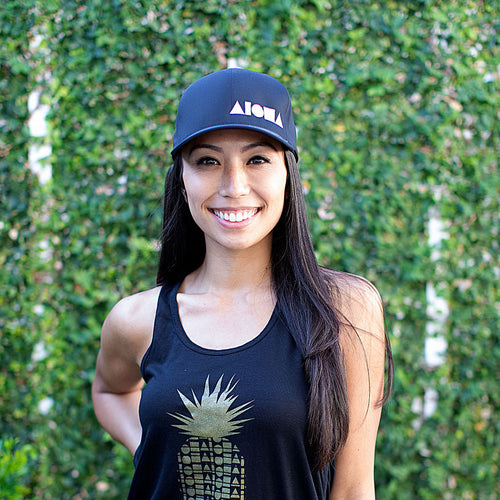 Smiling woman wearing Adult Flexfit curved bill hat. Black with white embroidered ALOHA Shapes ® logo. 
