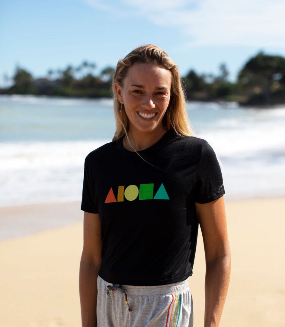 Woman on beach in Maui wearing womens Rainbow Aloha Shapes® logo flowy crop tee