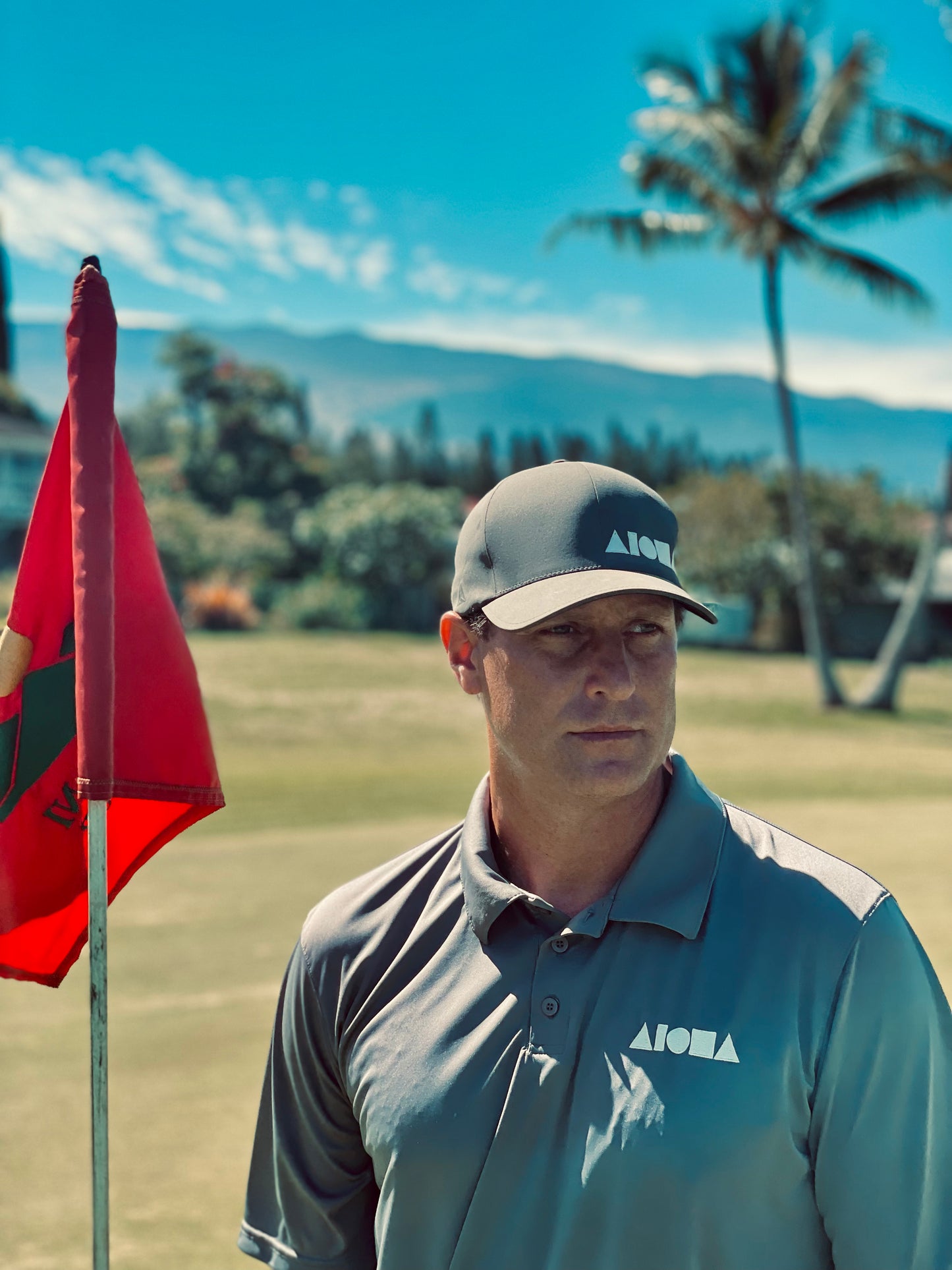 Person standing by a golf flag on the green wearing an embroidered Aloha Shapes® collared polo shirt
