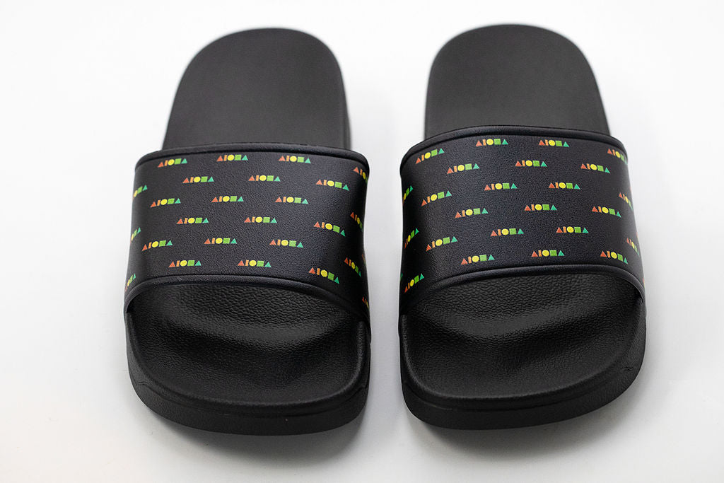 PVC slide-on slippers printed on top strap with repeating Aloha Shapes® logo in rainbow colors