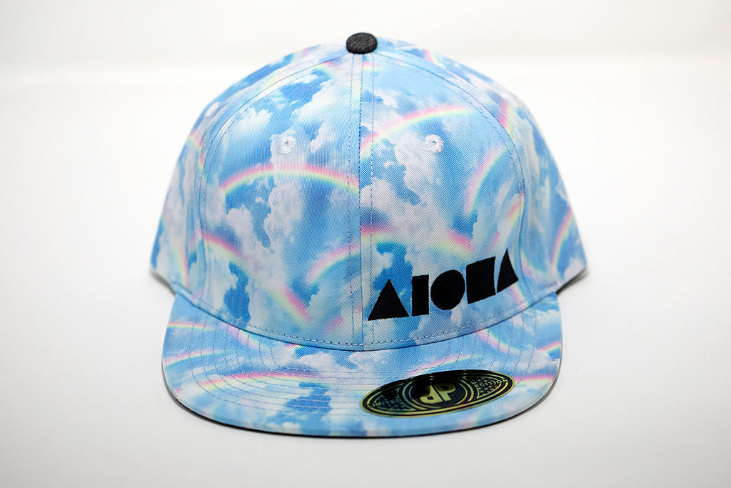 Adult flat brim snapback hat printed with rainbows and clouds. Embroidered in Maui Hawaii with black Aloha Shapes logo