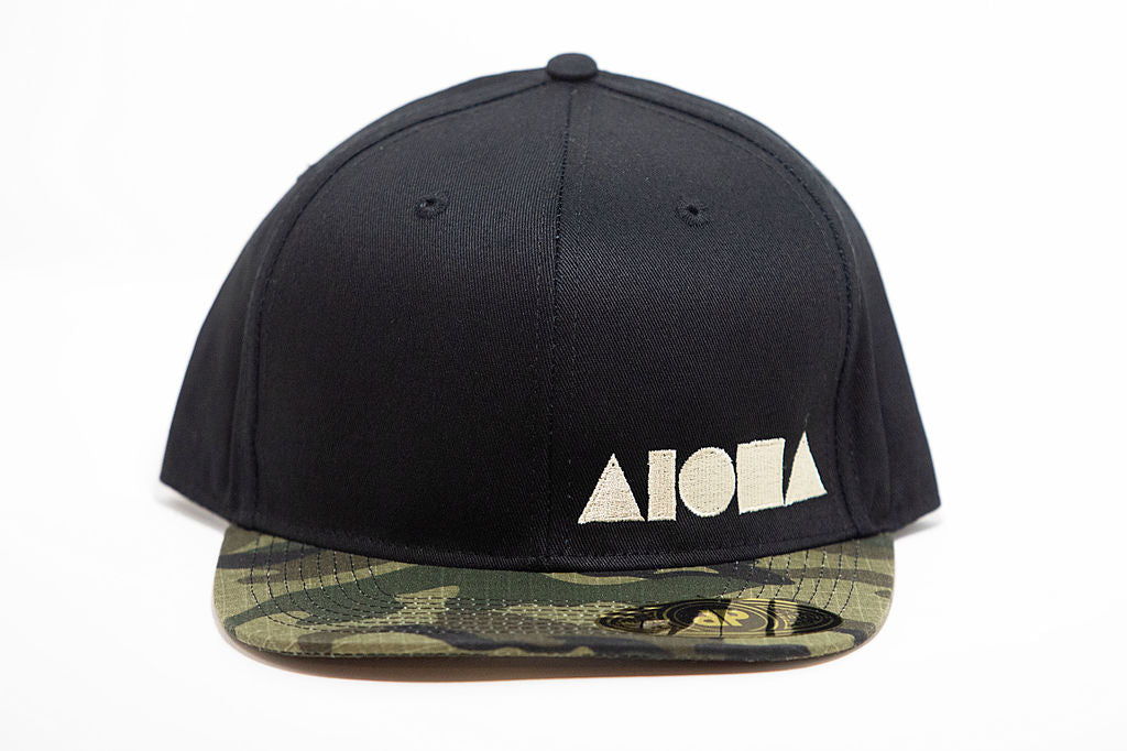 Black adult flat brim snapback hat embroidered with tan Aloha Shapes ® logo and a camo brim