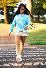 Woman walking across a crosswalk wearing Sync Aloha Surf Shapes longsleeve hoodie rashguard