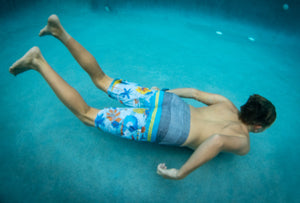 Young person wearing "Domes" Aloha Surf Shapes boardshorts standing in a pool in Maui Hawaii swimming underwater