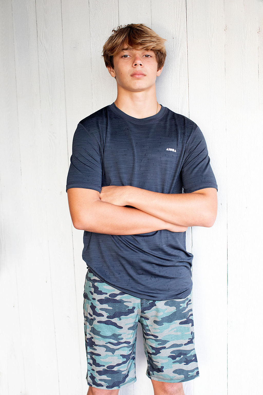 Young man wearing camo print unisex youth boardshorts with arms crossed