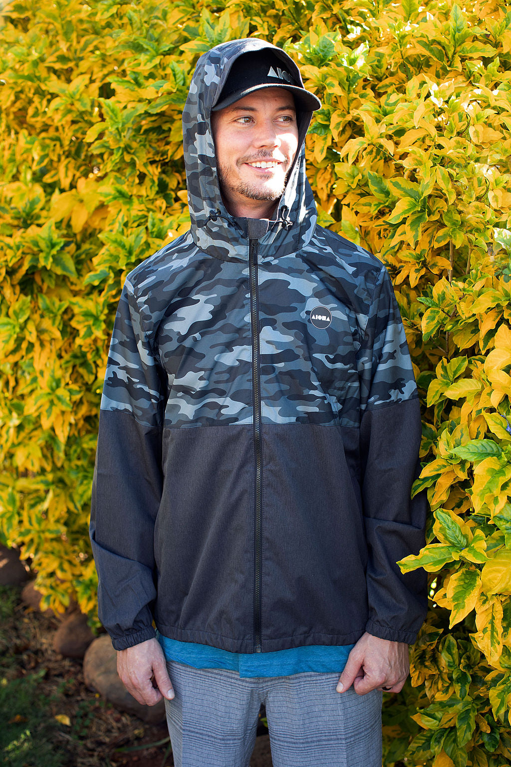 Man wearing Aloha Surf Shapes "Major" rain jacket in front of tropical plants