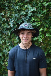 Young man wearing a camo print Aloha Surf Shapes "Watson" boonie hat