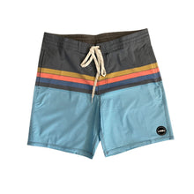 Adult surf shorts with dark grey waistband, horizontal blue, pink and yellow stripes and light blue legs. Aloha Surf Shapes fabric logo on left leg