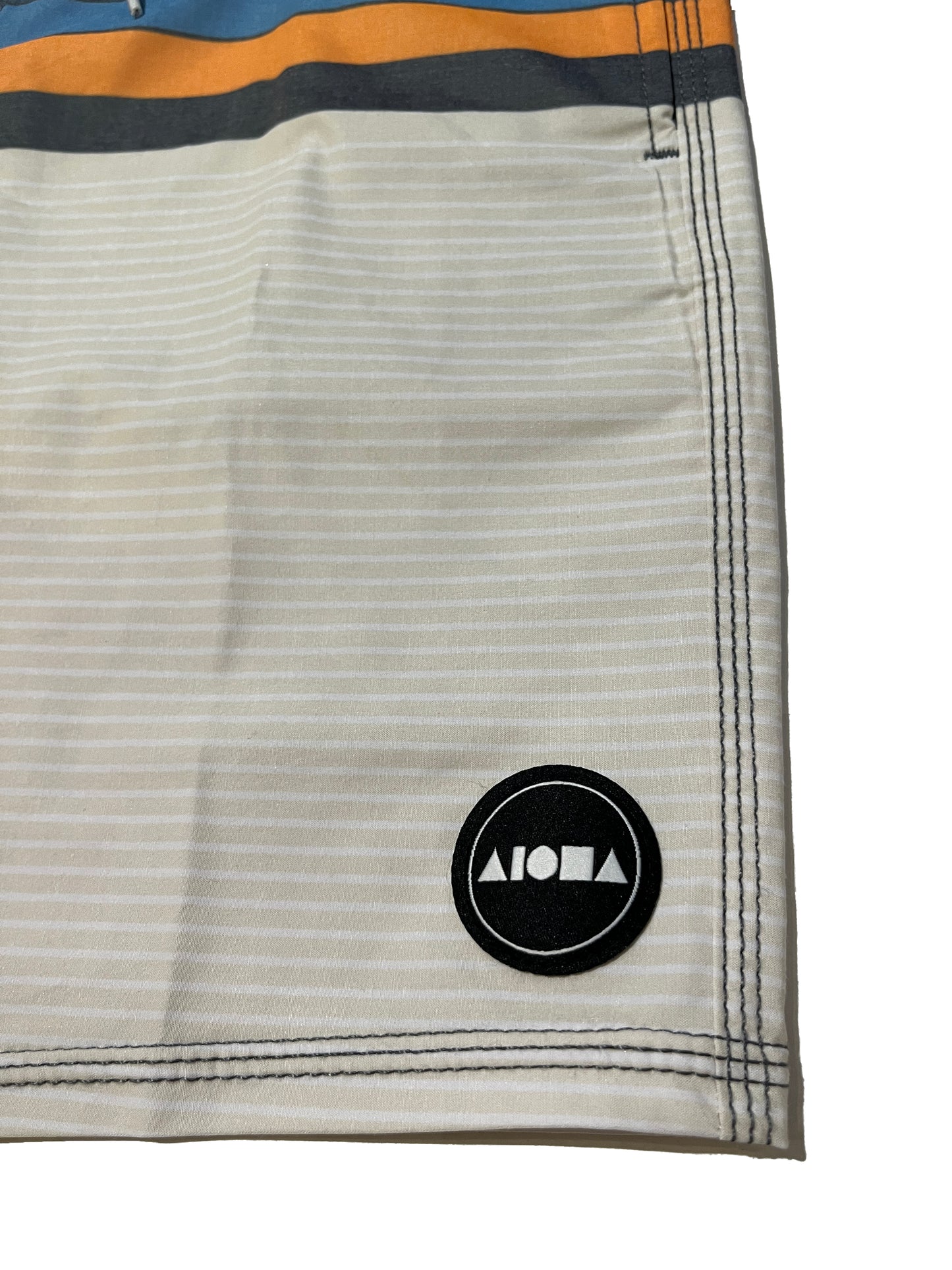 Closeup detail of Aloha Surf Shapes boardshorts woven logo on left leg