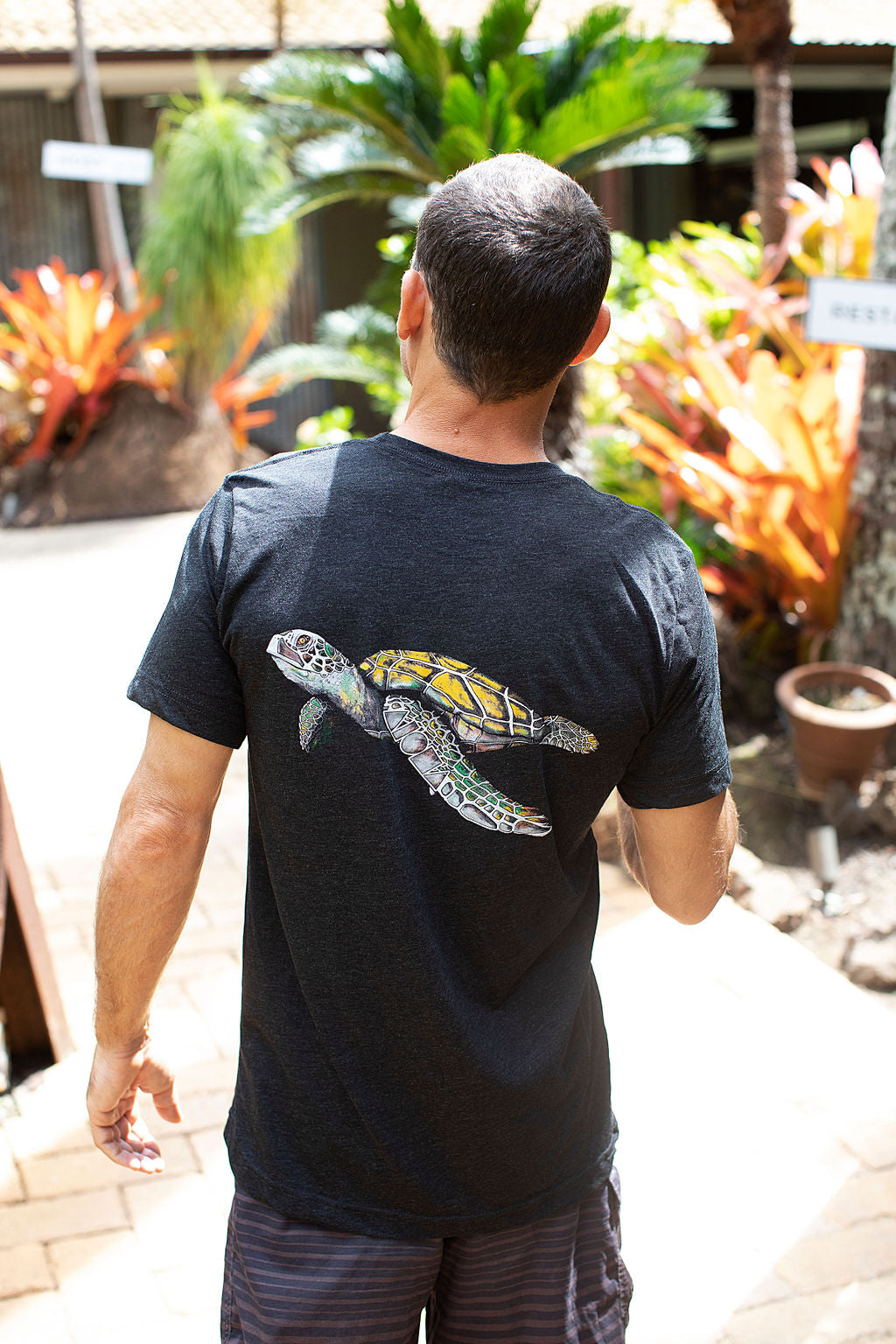 man walking through a garden with his back turned showing the Aloha Shapes ® Turtle design on his tshirt