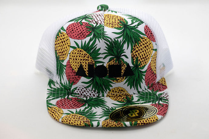 Youth flat brim snapback hat with pink and yellow pineapples on white background embroidered with black Aloha Shapes logo